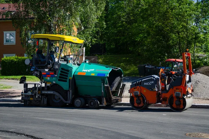 Mesin asphalt paver Vögele Super 1303-3i dan tandem roller pemadat aspal terparkir di tepi badan jalan baru dengan hamparan aspal hotmix hitam rapi