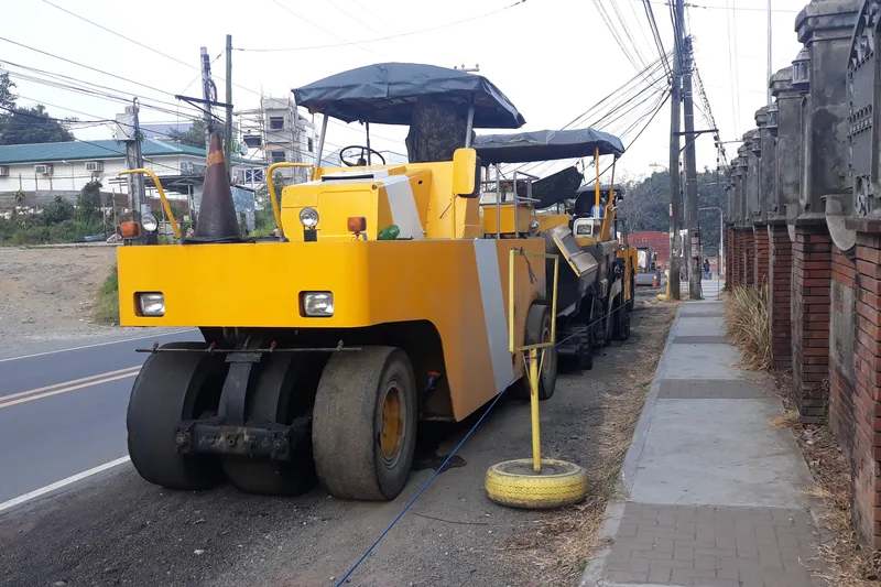 Unit mesin pemadat roda karet pneumatic tire roller dan asphalt paver crawler terparkir di bahu jalan koridor arteri dua lajur siap pelaksanaan penghamparan aspal hotmix