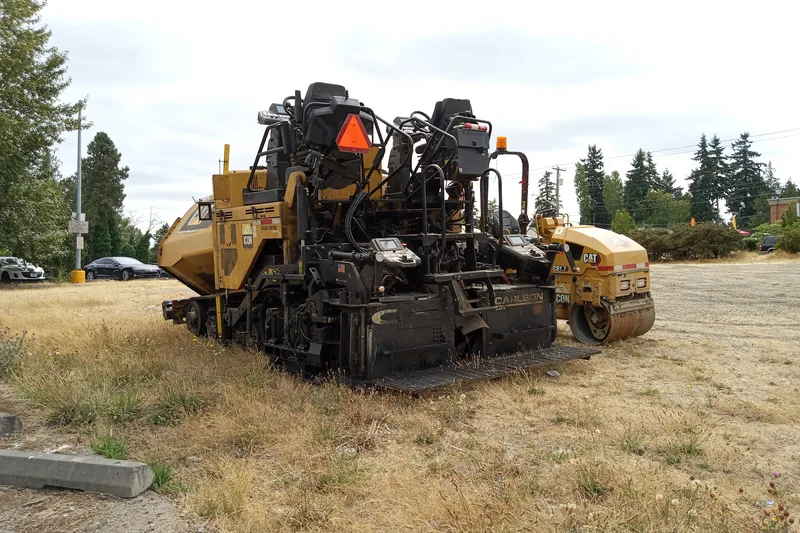 Unit mesin crawler asphalt paver berpengarah screed Carlson dan tandem roller pemadat jalan Caterpillar di area penyiapan proyek perkerasan jalan